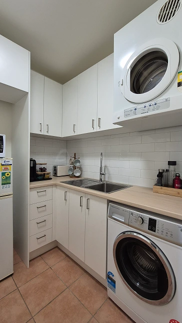 Renovated kitchenette and laundry in Aberfeldie featuring white cabinets, wooden countertops, and integrated appliances