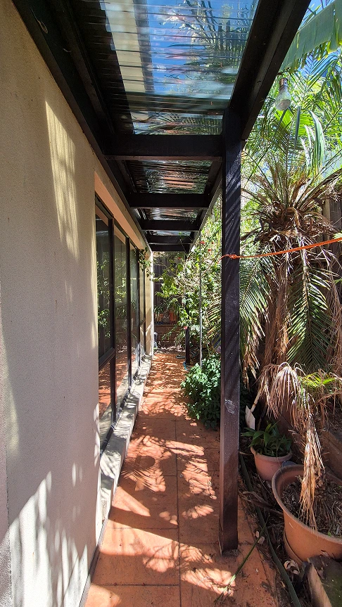 Renovated pergola at Aberfeldie featuring black beams, new glass roofing, and tropical garden setting