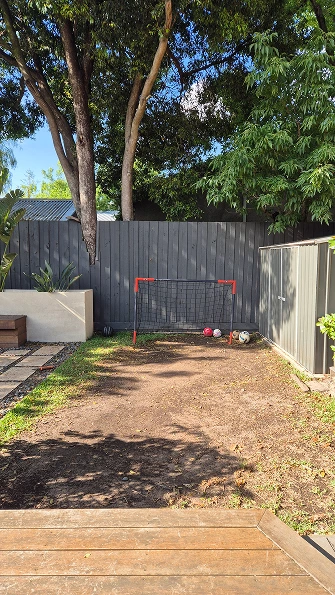 Backyard in Camberwell before landscaping showing bare ground, charcoal fence, soccer goal, and existing trees.
