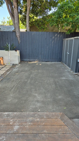 Finished concrete slab in Camberwell backyard showing smooth grey surface against charcoal fence and storage shed.
