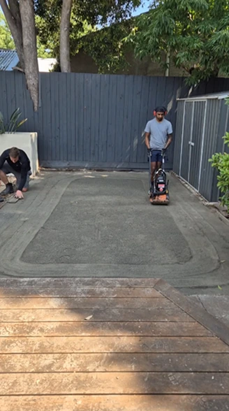 Concrete base preparation in Camberwell backyard with workers compacting the surface for landscaping project.