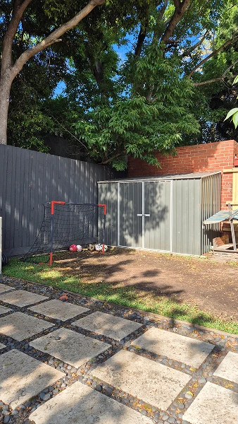 Camberwell backyard during landscaping renovation showing pavers, storage shed, and existing play area with soccer goal.