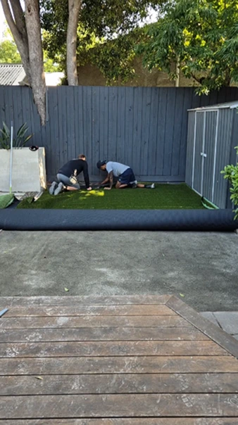 Workers installing artificial turf in Camberwell backyard over concrete base, showing transformation in progress.
