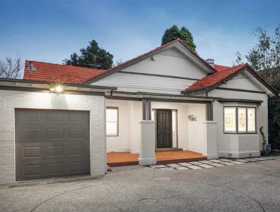 Evening view of renovated Camberwell home featuring white brick exterior, timber porch, and illuminated entrance.