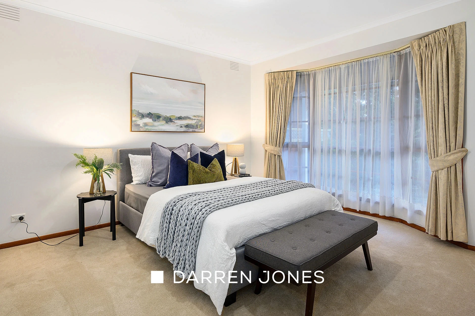 Modern bedroom with grey bed, landscape art and cream curtains