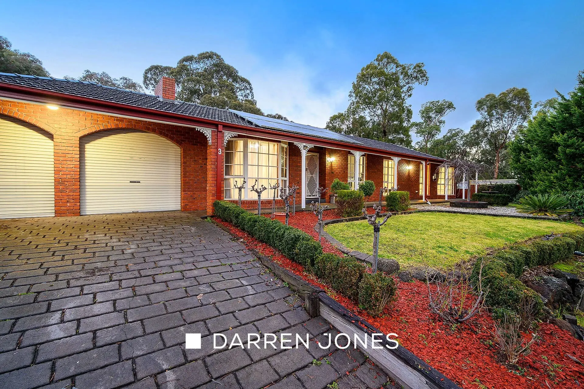 Ranch-style brick home with veranda and landscaped gardens at dusk