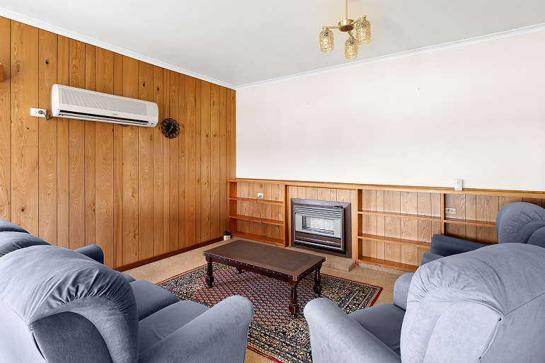 Living room before renovation in Mt. Gambier with wood paneling, built-in shelving, and gas fireplace insert