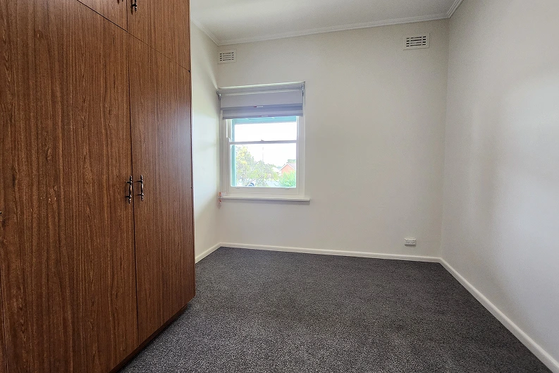 Renovated second bedroom in Mt. Gambier with new carpet, modern blind, and retained wooden wardrobe