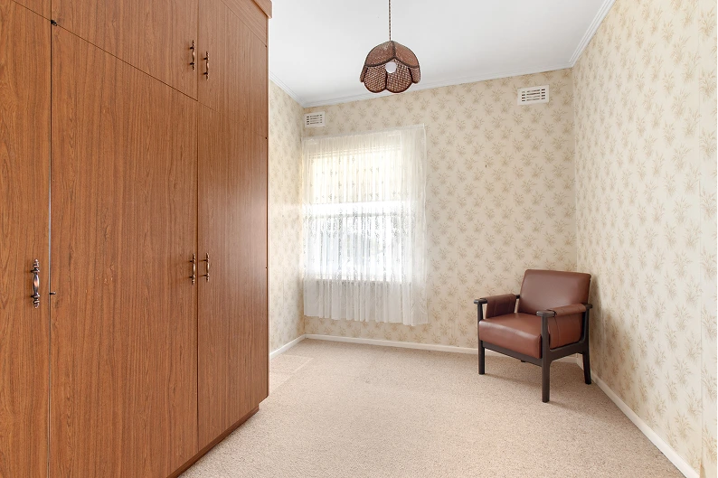 Second bedroom before renovation in Mt. Gambier with built-in wardrobe, wallpaper, and vintage armchair
