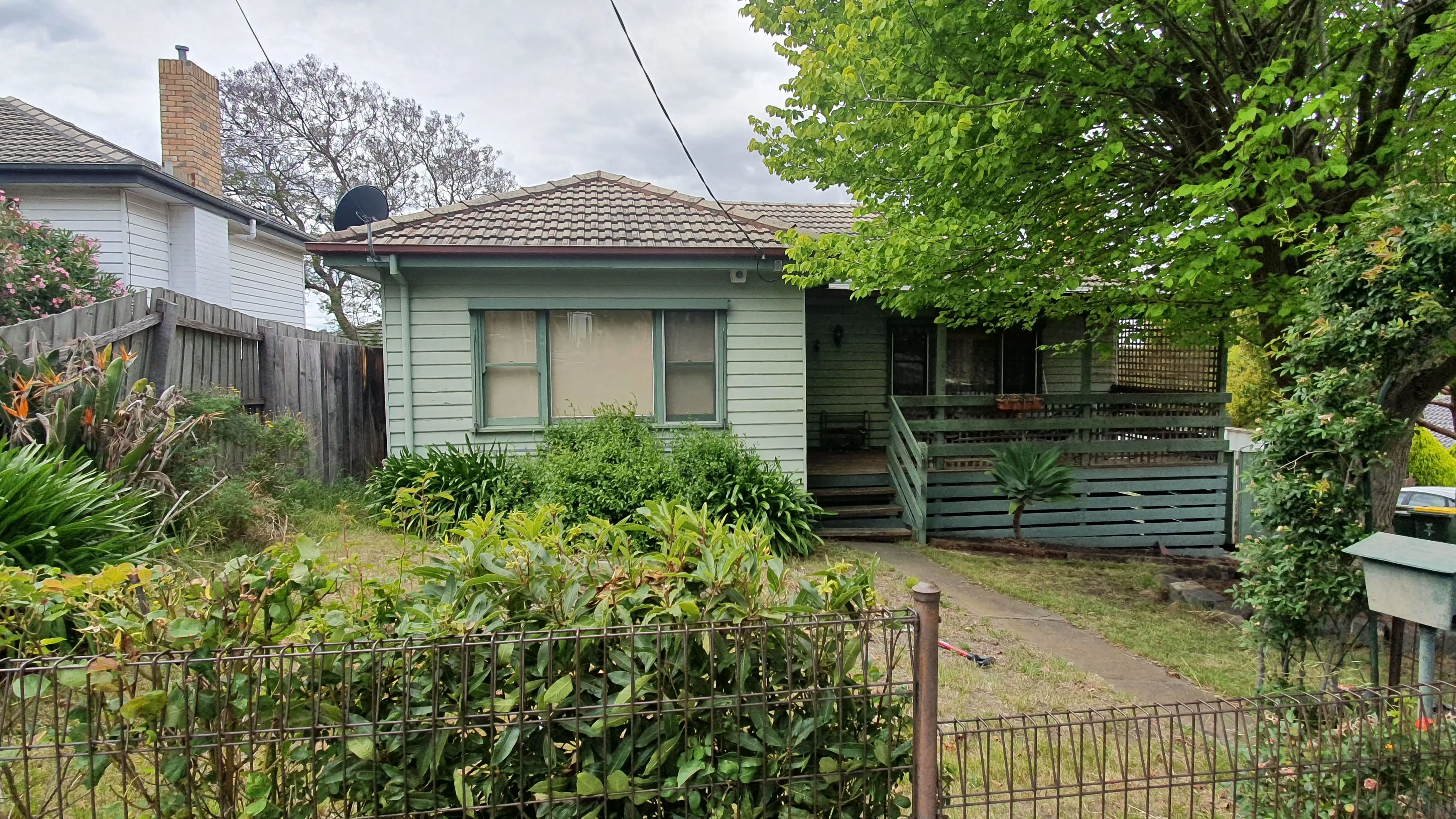 Green weatherboard house with renovation potential in Melbourne suburb