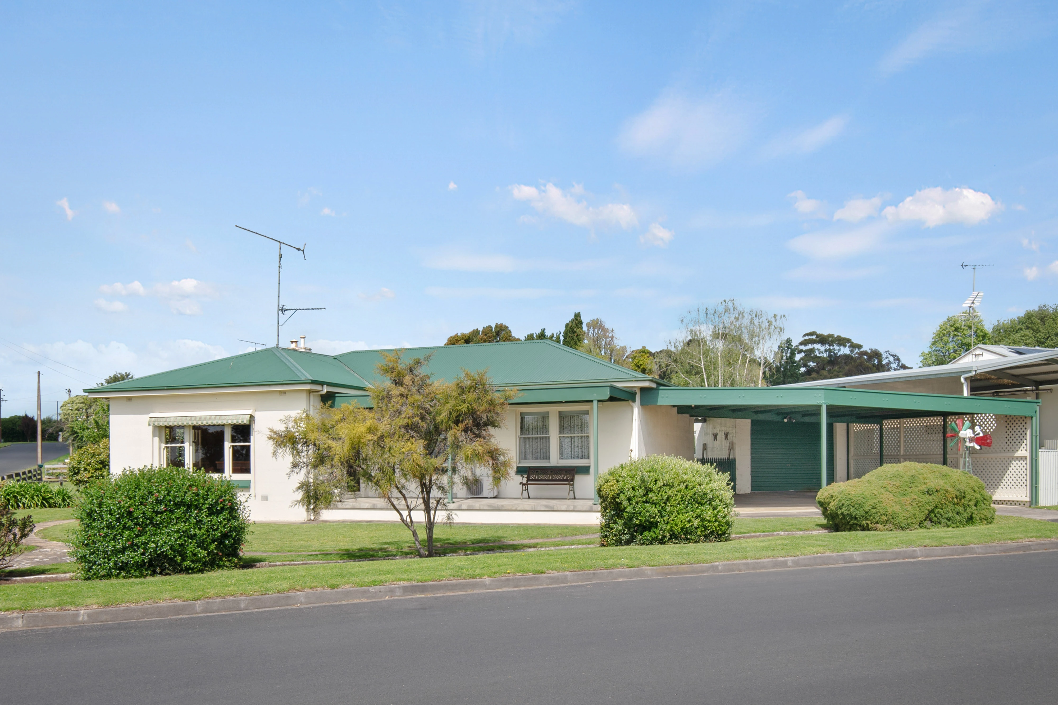 Cream house with green roof and established gard