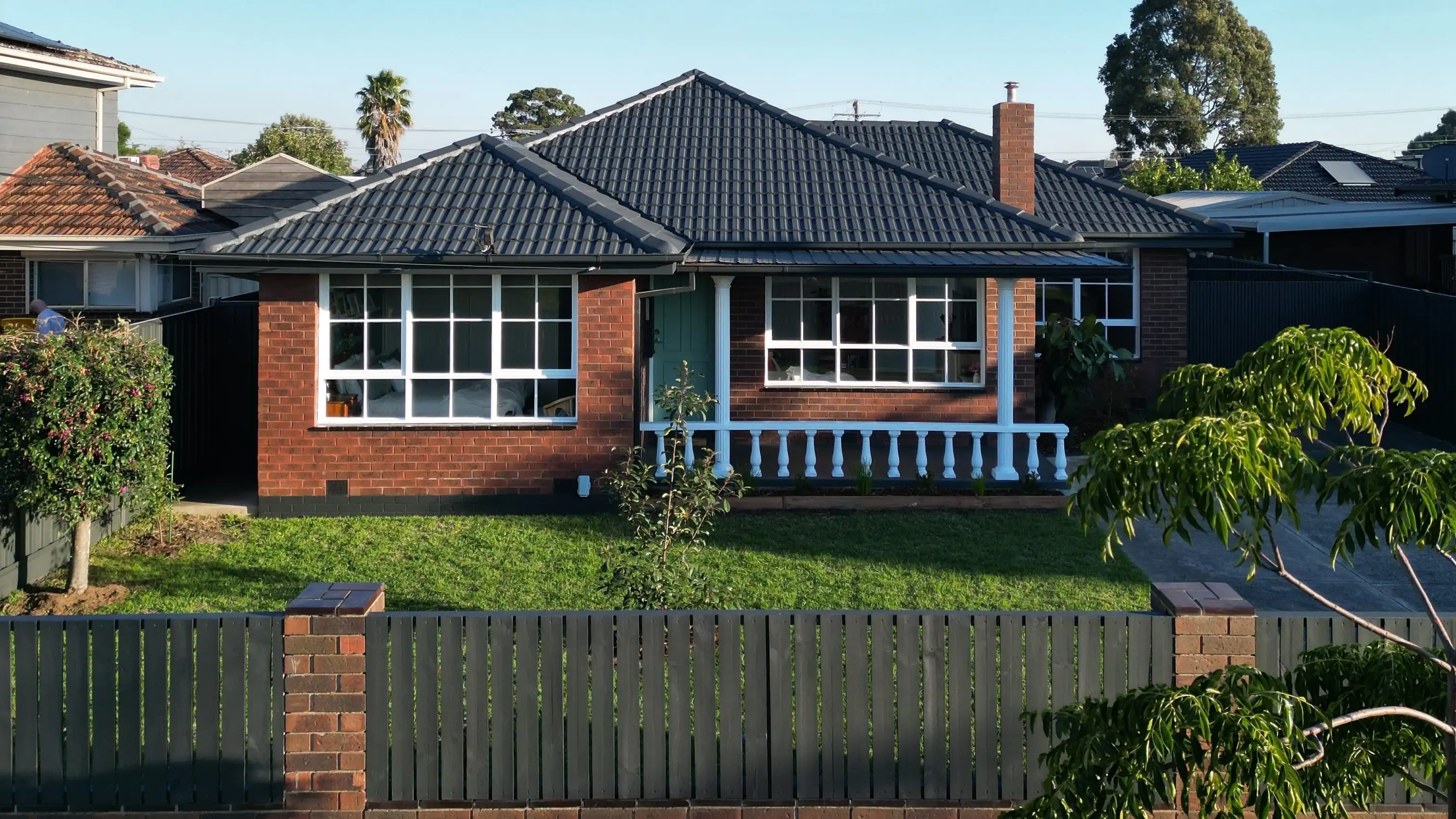 Renovated brick house with black roof and grey picket fence